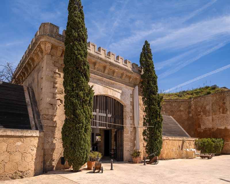 Portal de piedra flanqueado por cipreses en el patio del Hotel Cap Rocat