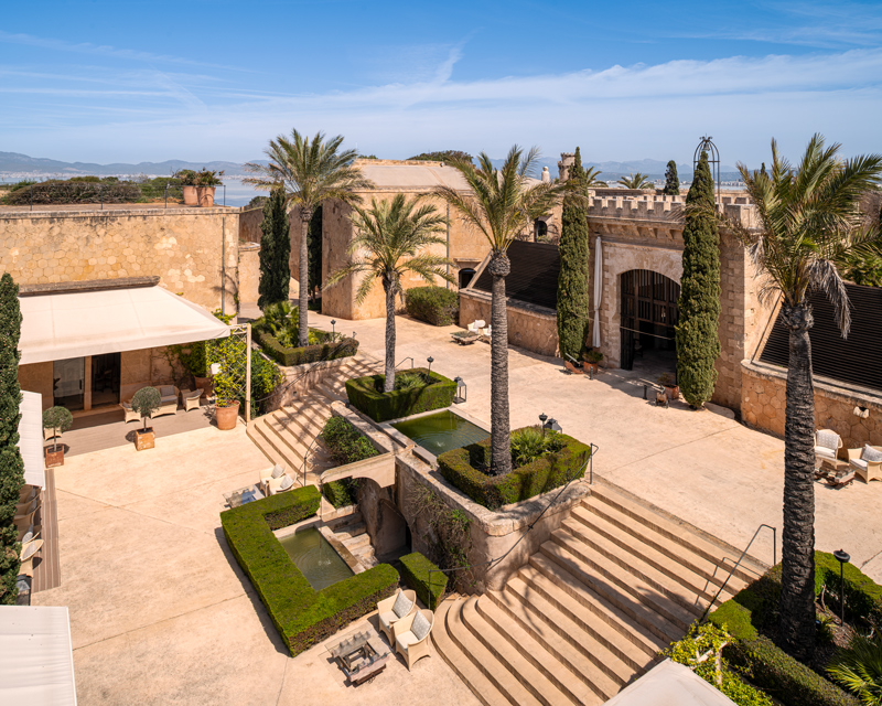 Vista elevada del patio de Cap Rocat, con palmeras, jardineras y escaleras de piedra